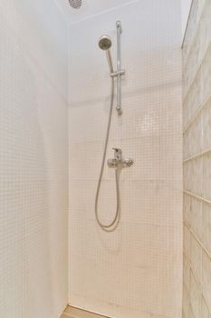 Shower faucet hanging on white tiled wall in light washroom in modern flat