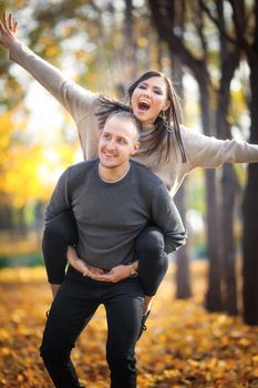 A young couple spends time together in nature. A man rides a woman on his back, and she depicts an airplane.