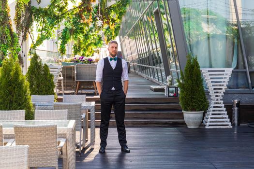 Young caucasian man in a suit with a bow tie in a summer street cafe.