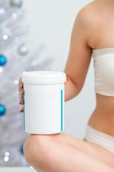 White plastic jar or container with blank empty space in hand of young woman on christmas tree background
