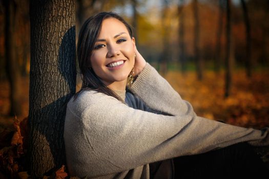 Young happy mixed race woman sitting on the grass in the park in autumn.