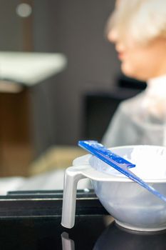 White hair dye in container on the special table on female customer background in hair salon
