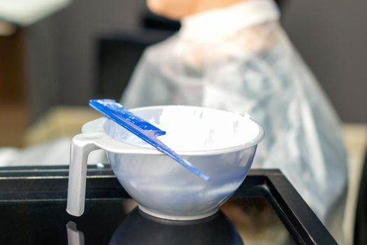 White hair dye in container on the special table on female customer background in hair salon