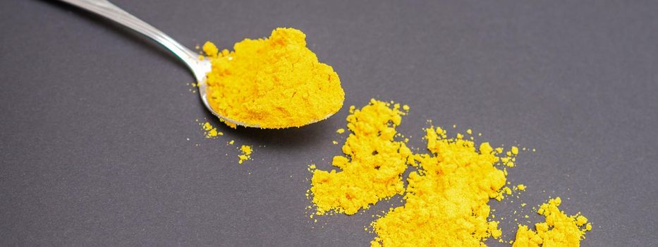 Turmeric or curcuma powder on metal spoon and scattered on dark background.