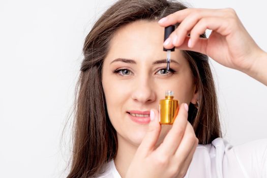 Portrait of smiling manicure master holds gold nail varnish bottle over her eye on white background