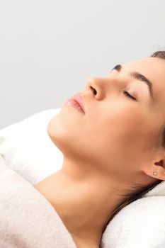 Side view of young woman lying on beautician table with closed eyes while waiting for cosmetic procedure in beauty salon