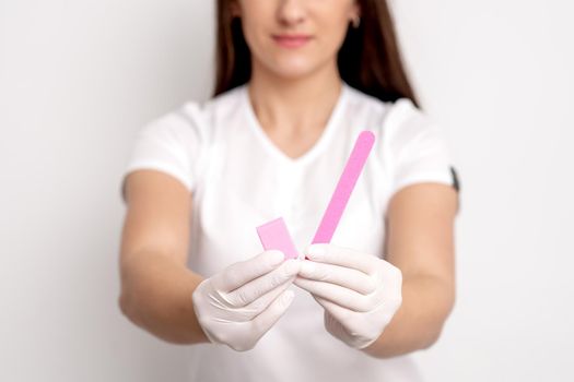 Manicure tools in hands of young female manicure master on white background. Selective focus