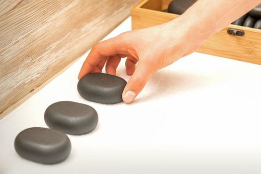 Hand of masseur lays out massage stones on the table in spa salon