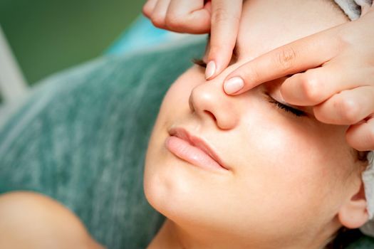 Young woman getting facial massage with closed eyes by beautician in beauty salon