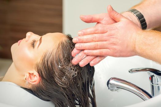 Beautiful young woman washing her hair by hands of male hairdresser in hair salon