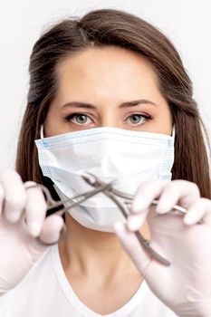 Portrait of manicure master with white protective mask holding manicure tools on white background