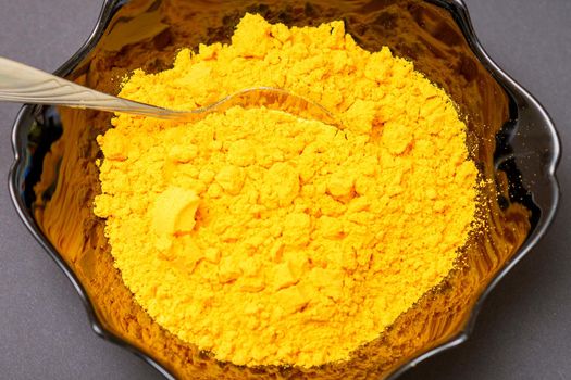 Top view closeup of turmeric or curcuma powder in ceramic black bowl or deep plate on dark background. Flat lay