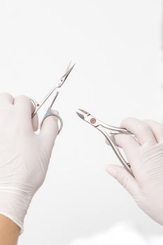 Manicure tools in hands of manicure master wearing white protective gloves on white background