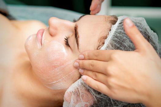 Young woman getting facial massage with closed eyes by beautician in beauty salon