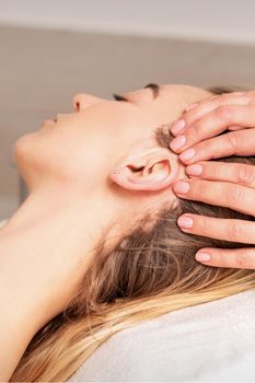 Young woman receiving head massage by hands of beautician in spa beauty center