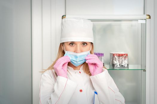 Female nurse or doctor wears protective gloves putting on medical face mask in the lab