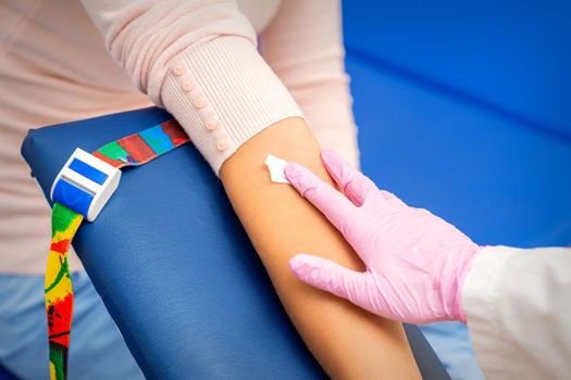 Hand of nurse applying cotton swab to arm of young woman after blood sample in the hospital