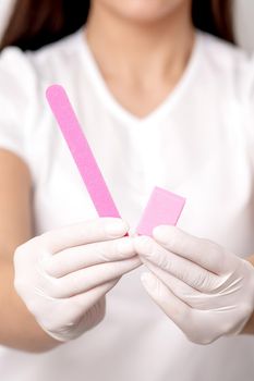 Manicure tools in hands of young female manicure master on white background. Selective focus