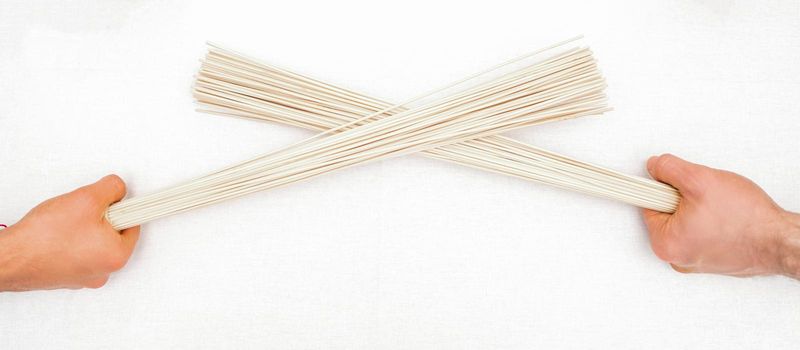 Bamboo massage brooms in hands of two masseurs isolated on white background