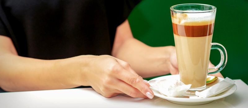 Close up of female waiter gives cup of coffee latte with candy in plate on the table