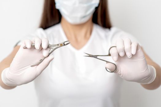 Manicure tools in hands of female manicurist wearing white mask and gloves on white background