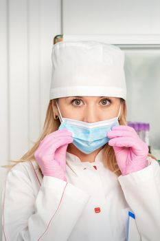Female nurse or doctor wears protective gloves putting on medical face mask in the lab