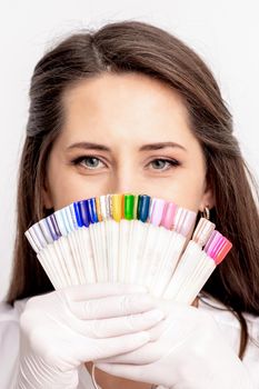 Portrait of female manicure master covering her face with nail sample palette on white background