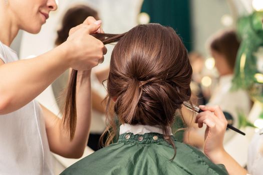 Makeup artist and hairdresser are preparing hairstyle and visage of young woman in beauty salon