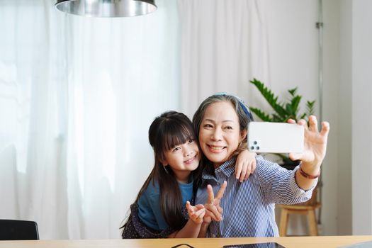 Asian portrait, grandma and granddaughter doing recreational activities using their phones to take selfies happily.