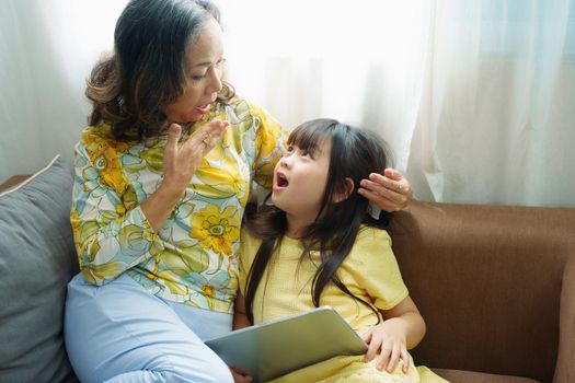 Asian portrait, Grandma and granddaughter doing recreational activities playing tablet computers on the sofa.