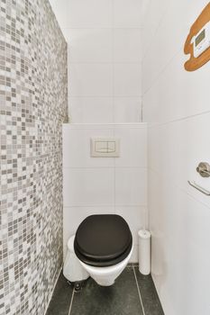 A modern toilet is installed on a white wall under a button in a light restroom with fine gray tiles.