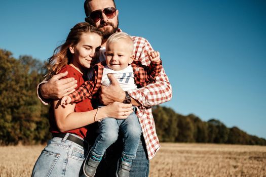 Happy Young Family Mom and Dad with Their Little Son Enjoying Summer Weekend Picnic Outside the City in Field at Sunny Day Sunset, Vacation Time Concept