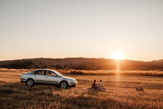 Happy Young Family Mom and Dad with Their Little Son Enjoying Summer Weekend Picnic on the Car Outside the City in Field at Sunny Day Sunset, Vacation and Road Trip Concept