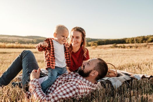 Happy Young Family Mom and Dad with Their Little Son Enjoying Summer Weekend Picnic Outside the City in Field at Sunny Day Sunset, Vacation Time Concept