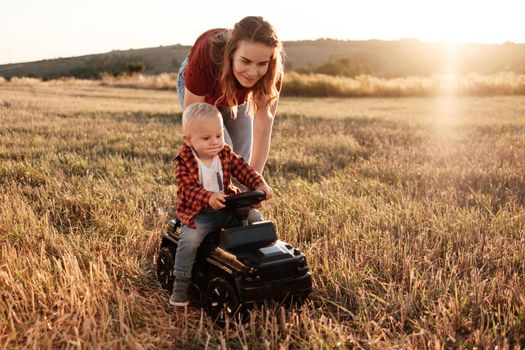 Happy Mom with Her Little Son Enjoying Summer Weekend Outside the City in Field at Sunny Day Sunset