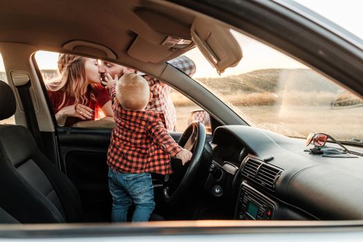 Happy Young Family Mom and Dad with Their Son Little Driver Enjoying Summer Weekend Picnic on the Car Outside the City in Field at Sunny Day Sunset, Vacation and Road Trip Concept