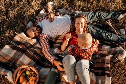 Happy Young Family Mom and Dad with Their Little Son Enjoying Summer Weekend Picnic Outside the City in Field at Sunny Day Sunset, Vacation Time Concept