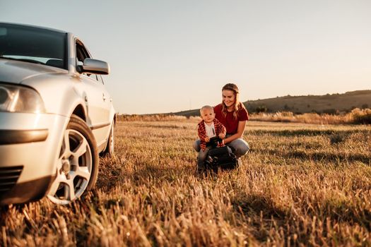 Happy Mom with Her Little Son Enjoying Summer Weekend Outside the City in Field at Sunny Day Sunset