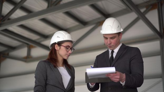 Young man and woman in helmets with documents at a construction site. Businessmen in suits conclude an agreement. A man signed documents. 4k