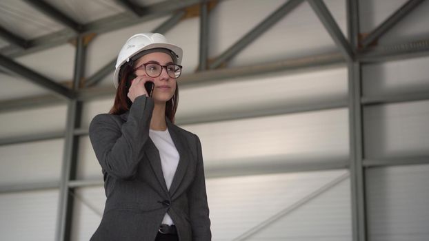 A young woman in a helmet speaks on the phone at a construction site. The boss in a suit is talking on the phone. 4k