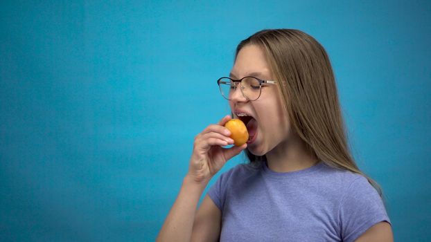 Teenager girl with braces on her teeth eats an apricot on a blue background. Girl with colored braces bites off an apricot. 4k