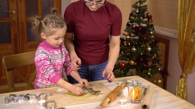 A daughter with a young mother makes a traditional festive Christmas cookies in the form of a deer. A figurine is placed in the dough. 4k