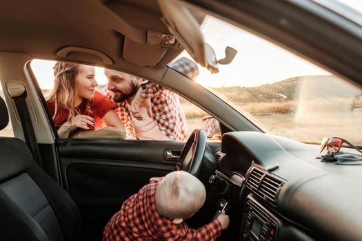 Happy Young Family Mom and Dad with Their Son Little Driver Enjoying Summer Weekend Picnic on the Car Outside the City in Field at Sunny Day Sunset, Vacation and Road Trip Concept