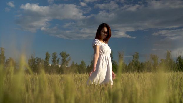 A young woman in a white dress walks on a green wheat field. View of the girl through the spikelets. 4k