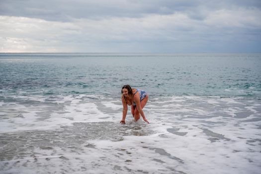 A plump woman in a bathing suit enters the water during the surf. Alone on the beach, Gray sky in the clouds, swimming in winter