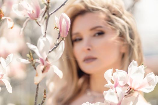 Portrait of a beautiful happy middle aged woman enjoying the smell in a blooming spring garden. Beautiful magnolia bushes, large flowers