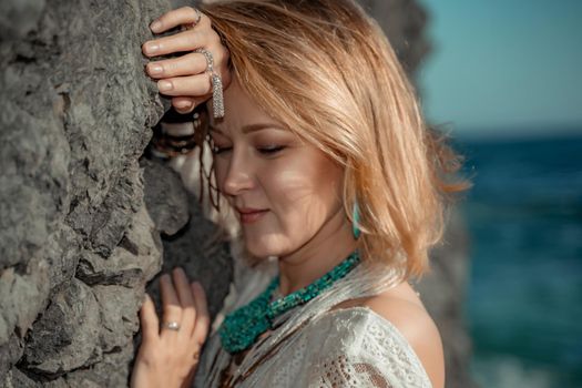 Middle aged woman looks good with blond hair, boho style in white long dress on the beach decorations on her neck and arms