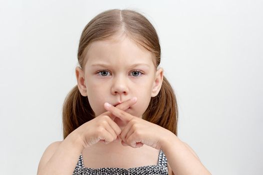 Caucasian serious little girl of 6 years crossed fingers on mouth showing speechless and voiceless