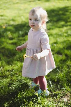 Little girl in a field, child with dandelion flower in park in summer. Happy kid having fun outdoors