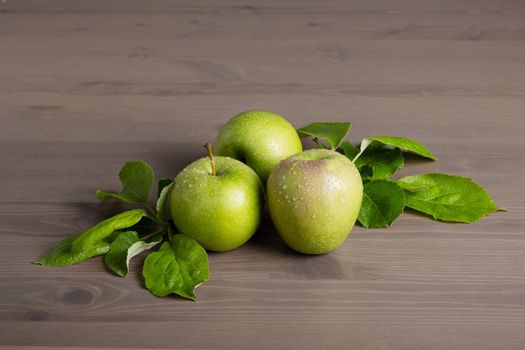 Top view of a composition of fresh ripe green apples and apple tree leaves on a wooden background. Selective focus.